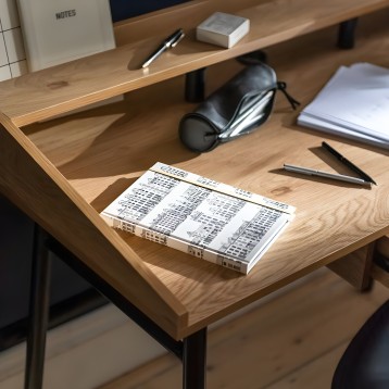 Escritorio de madera clara con patas metálicas negras y estante superior integrado en ambiente de oficina