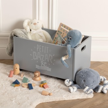 Caja de almacenamiento gris con asas y texto decorativo llena de juguetes y peluches infantiles en ambiente de habitación