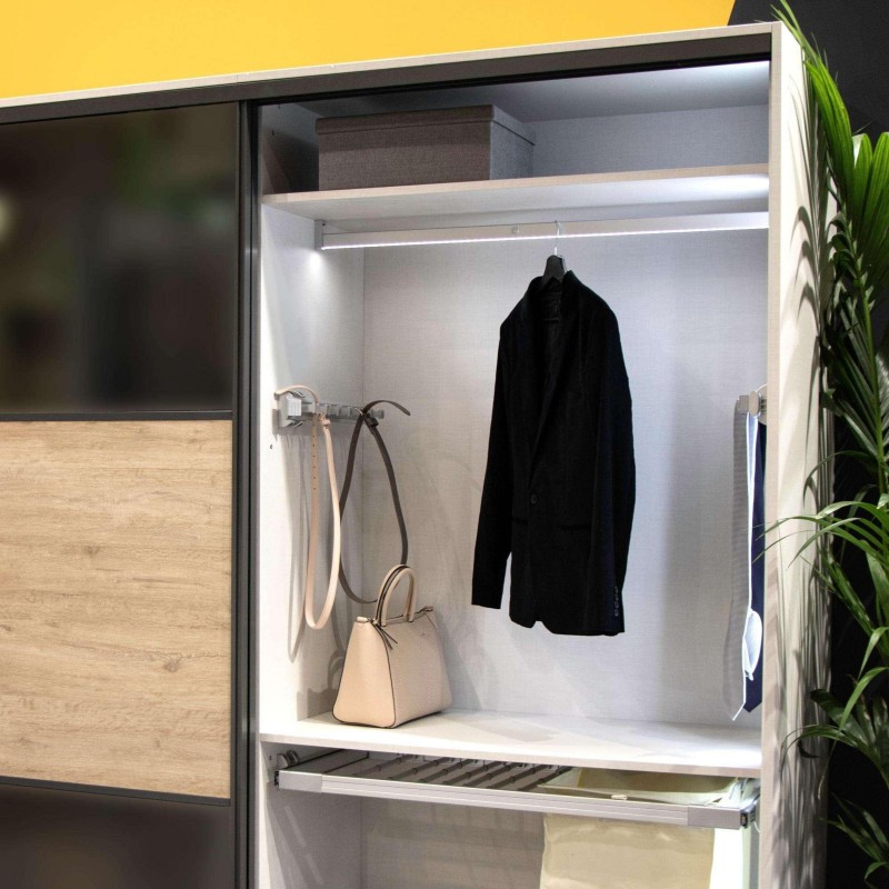 Armario con puertas correderas de madera y vidrio con interior iluminado y barra de colgar ropa y estantes
