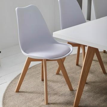 Silla de comedor con respaldo curvo blanco y asiento tapizado junto a mesa blanca y patas de madera natural