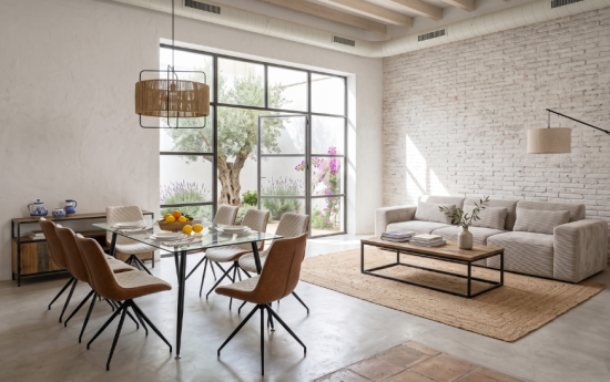 Mesa de comedor de cristal con sillas de piel marrón y sofá de pana beige en salón de estilo industrial